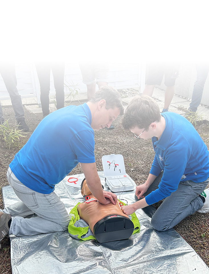 Zwei ODU-Mitarbeiter knien am Boden und üben an einer Puppe eine Herzdruckmassage.